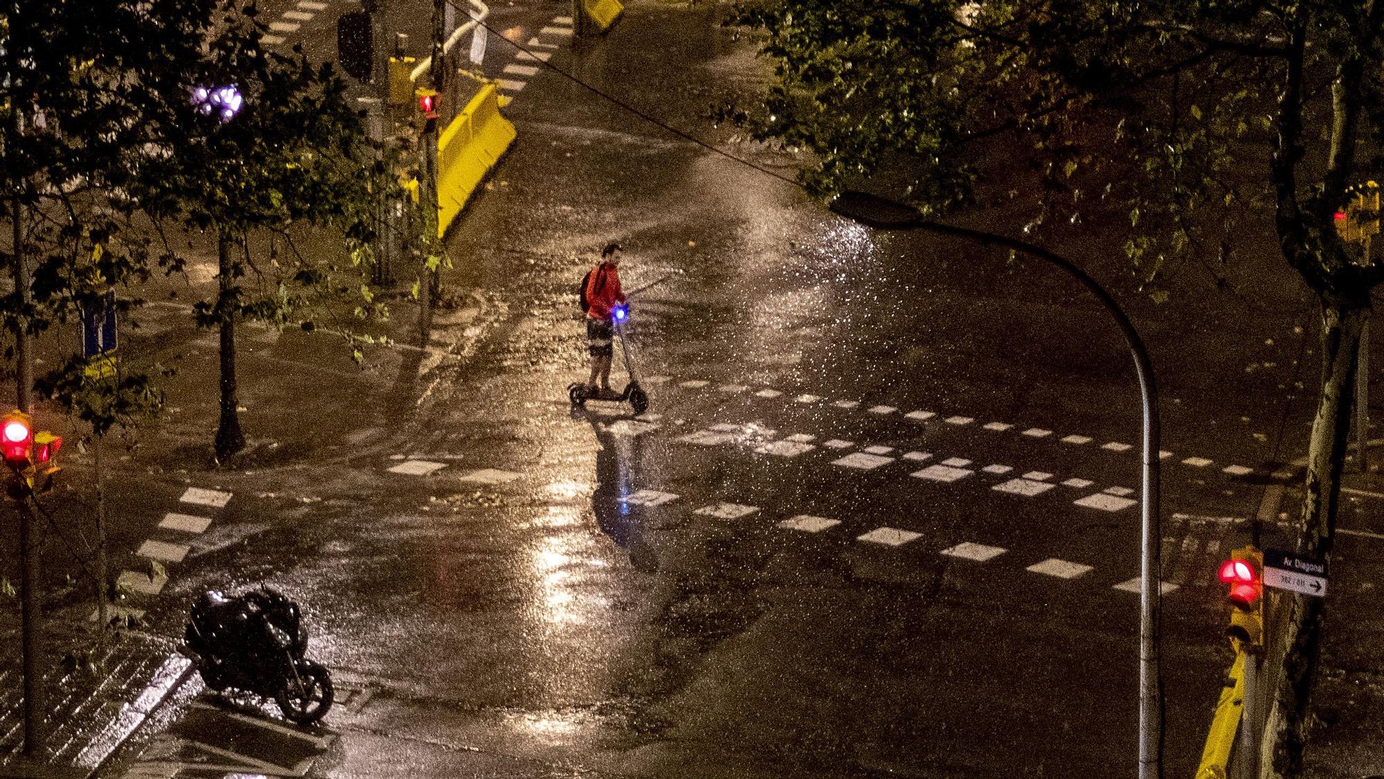 Un patinete cruza una de las calles del Eixample bajo la ligera lluvia de primera hora de la mañana