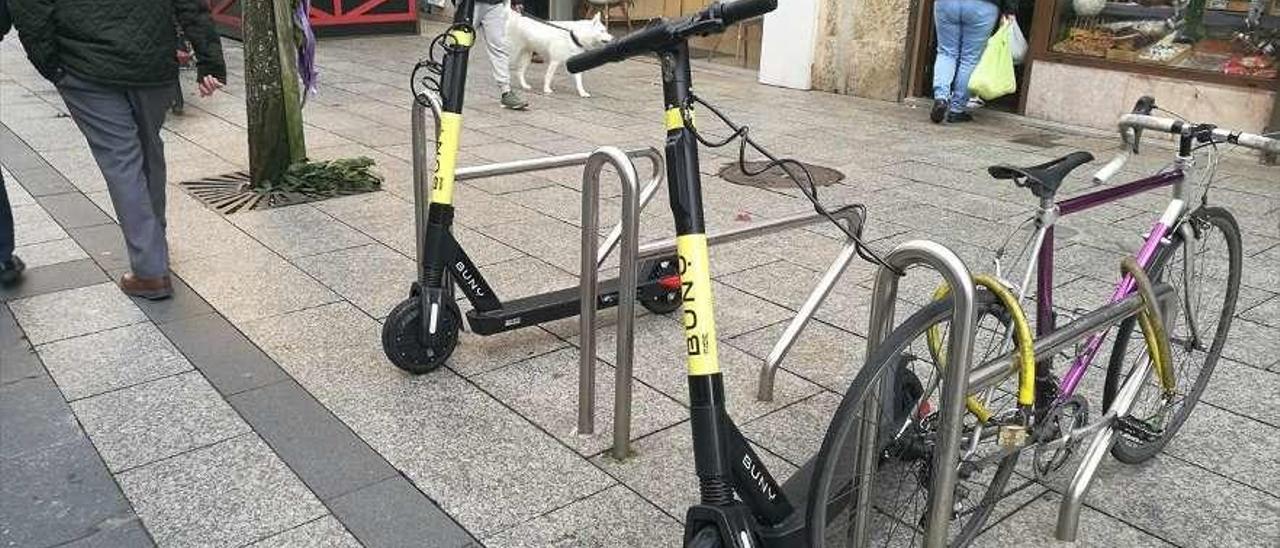 Dos de los patinetes eléctricos de alquiler que operan en Vigo anclados en un &#039;aparcabicis&#039; de O Calvario.