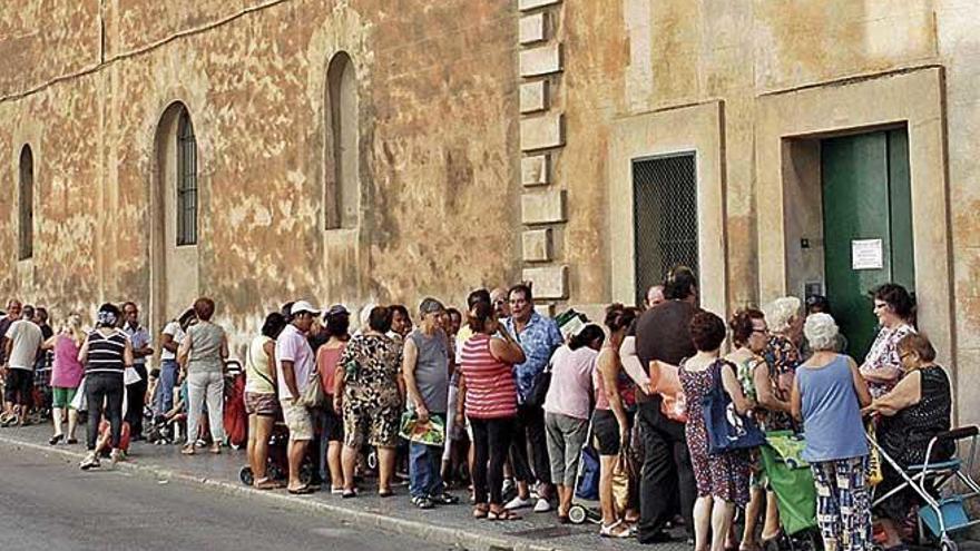 Gente haciendo cola en las puertas de la iglesia de los Caputxins pare recibir comida.