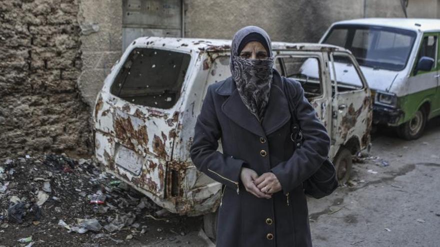 Una mujer junto a un coche tiroteado en Siria.