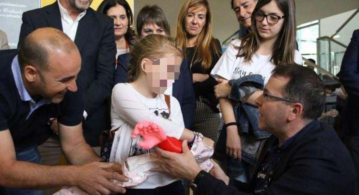 Momento de la entrega de la prótesis de brazo a la pequeña por parte de los dos profesores que la han diseñado
