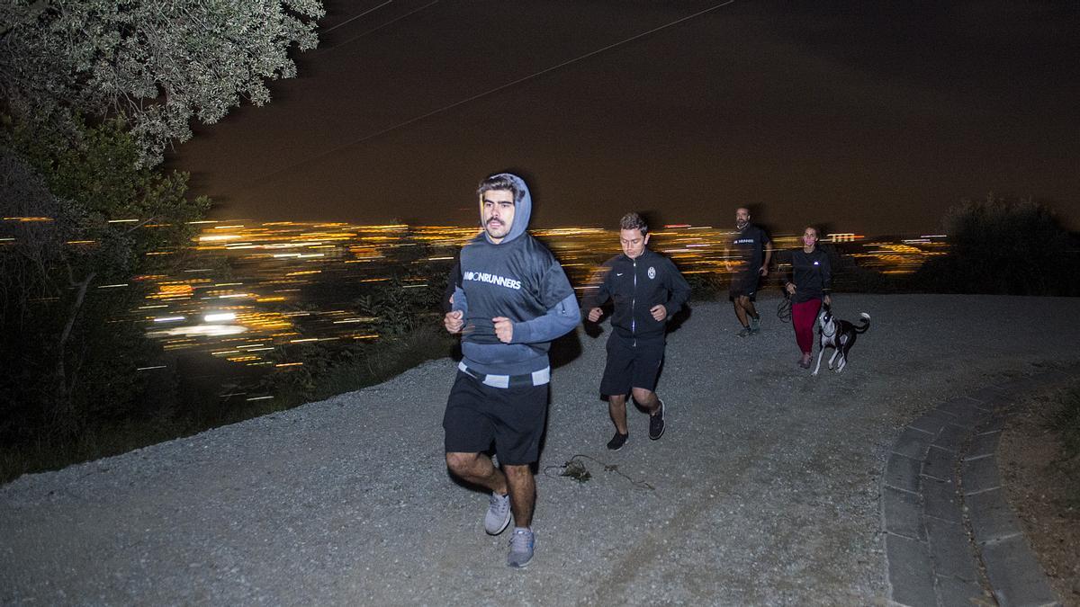 Un grupo de 'moonrunners' corren bajo la luna llena con Barcelona de fondo.