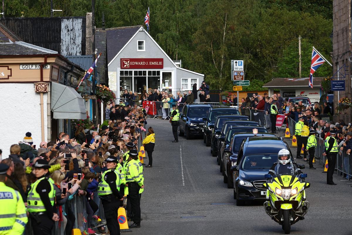 Largas filas de gente contemplan el paso del coche fúnebre con los restos de Isabel II en la localidad de Ballater, en Escocia.