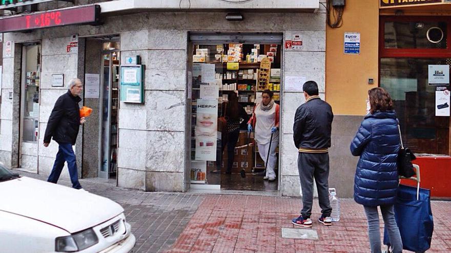 Clientes hacen cola en la puerta de una farmacia, manteniendo la distancia, en el centro de València.