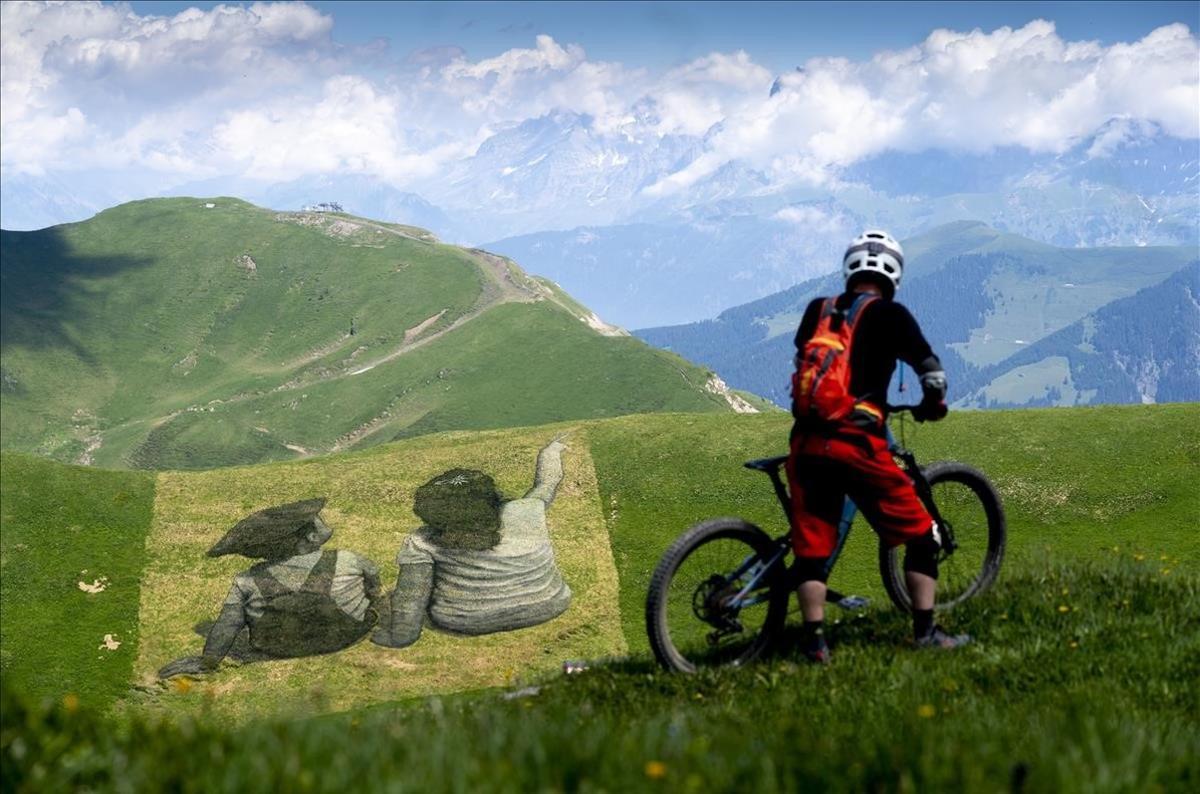 Un ciclista observa una pintura gigante del artista franco-suizo Saype llamada The Smugglers of Friendship!, frente a las montañas Les Dents du Midi en la zona de esquí suizo-francesa de Portes du soleil, en Les Crosets, Vall d’Illiez, Suiza. 