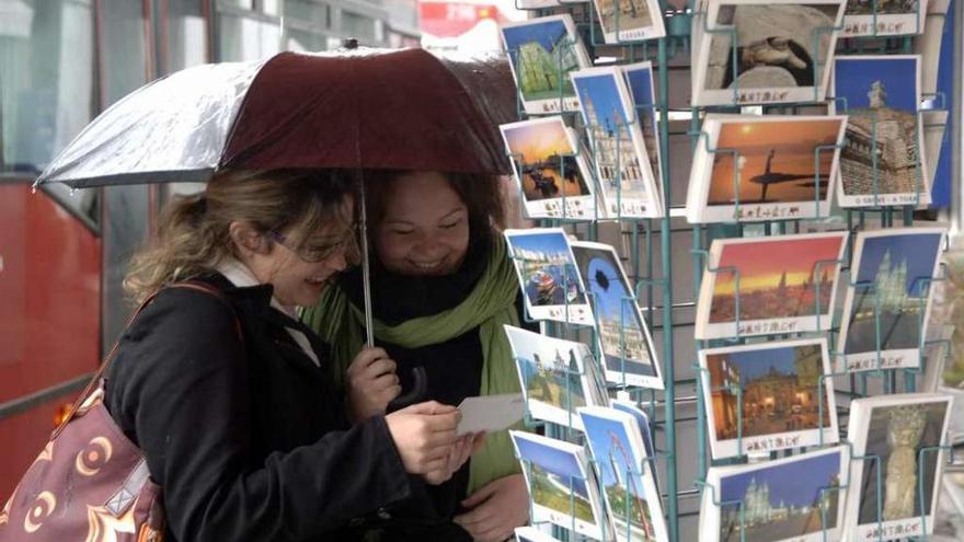 Dos turistas con paraguas observan en invierno postales turísticas de A Coruña.