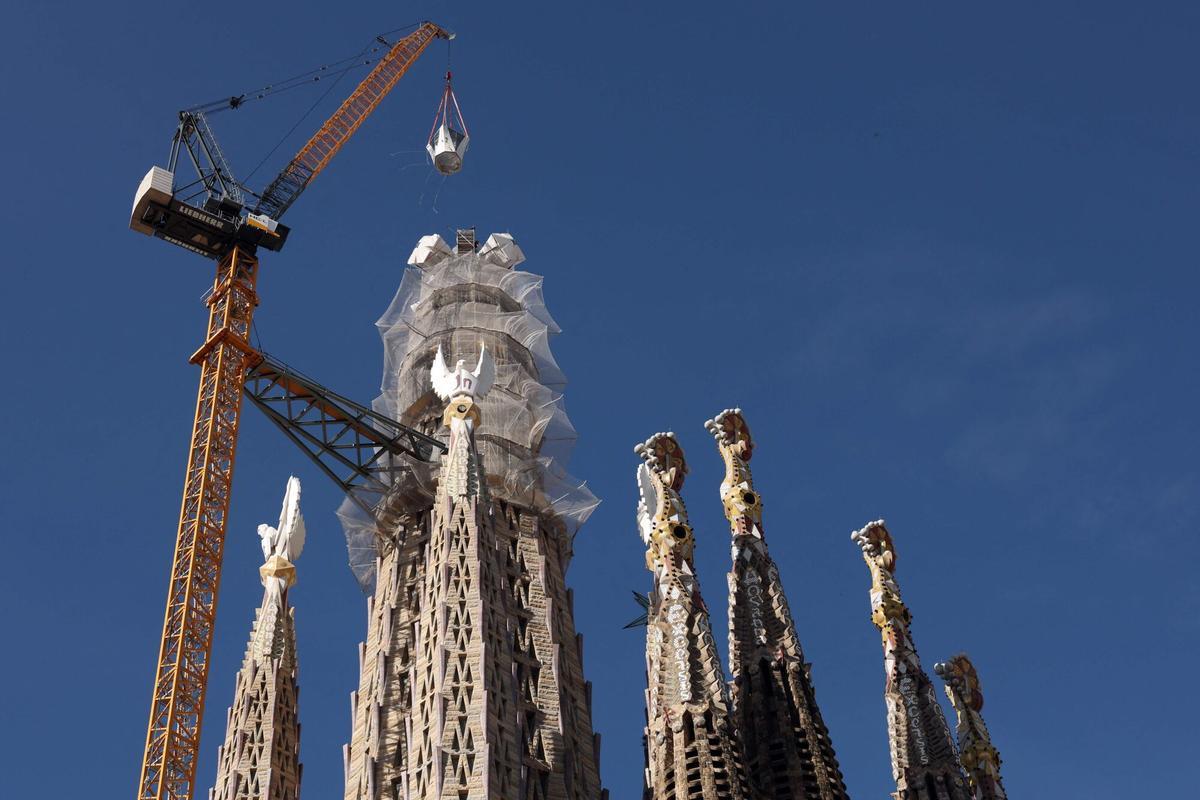 A crane lifts the final piece of the 17 meters high and 13.5 meters wide cross that completes the Sagrada Familia's Tower of Jesus Christ in Barcelona on February 20, 2026. The Sagrada Familia basilica reached its peak today after completing the cross on its central tower, which crowns the world's tallest church at 172.5 meters and represents a major step in the construction of the temple conceived by Antoni Gaudi more than 140 years ago. (Photo by Lluis GENE / AFP)