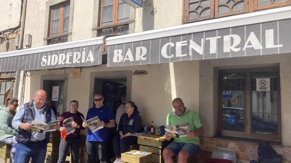 Varios vecinos leen la revista oficial de la Feria Capenastur, a las puertas del Bar Central, en Cornellana