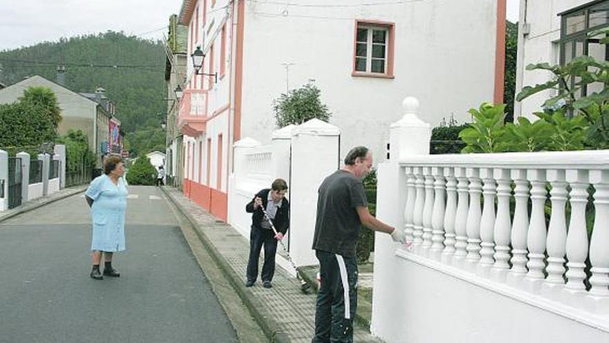 Carmen López barriendo la acera mientras Clemente Novo pinta la balaustrada de su vivienda, ayer, en San Tirso de Abres.