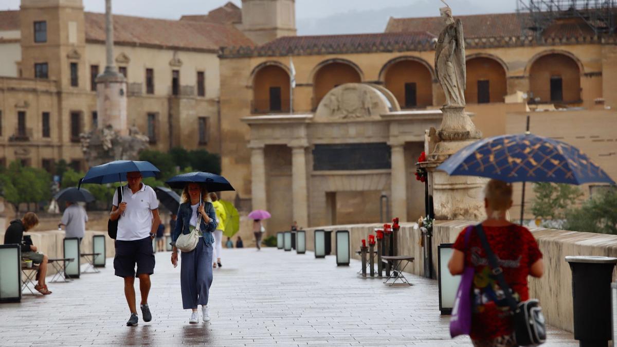 Varias personas caminan por el Puente Romano refugiadas bajo sus paraguas.