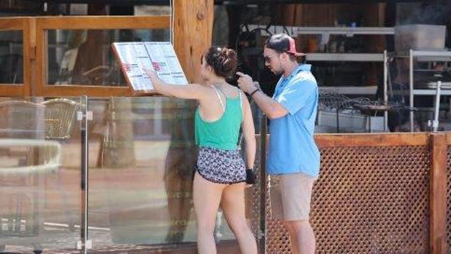 Dos turistas leen la carta de un restaurante de Platja d´en Bossa.