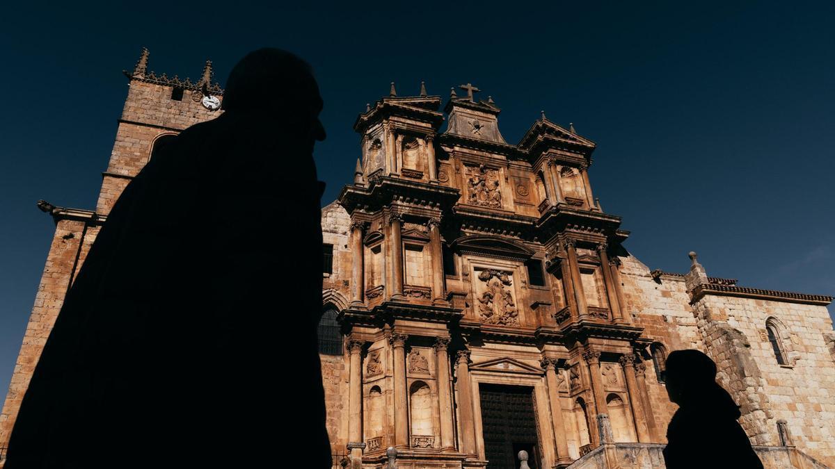 Dos turistas, a contraluz, observan la fachada de la Iglesia de Santa María de Gumiel de Izán, que se ha comparado al enclave arqueológico de Petra, en Jordania.