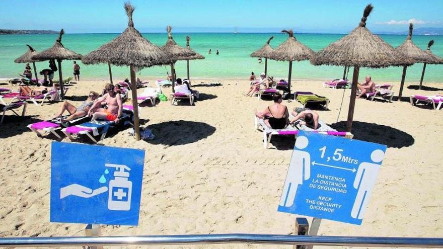 Turistas tomando el sol en una playa española, con los carteles en los que se recuerdan las medidas de seguridad en primer plano. | | JAIME REINA / AFP