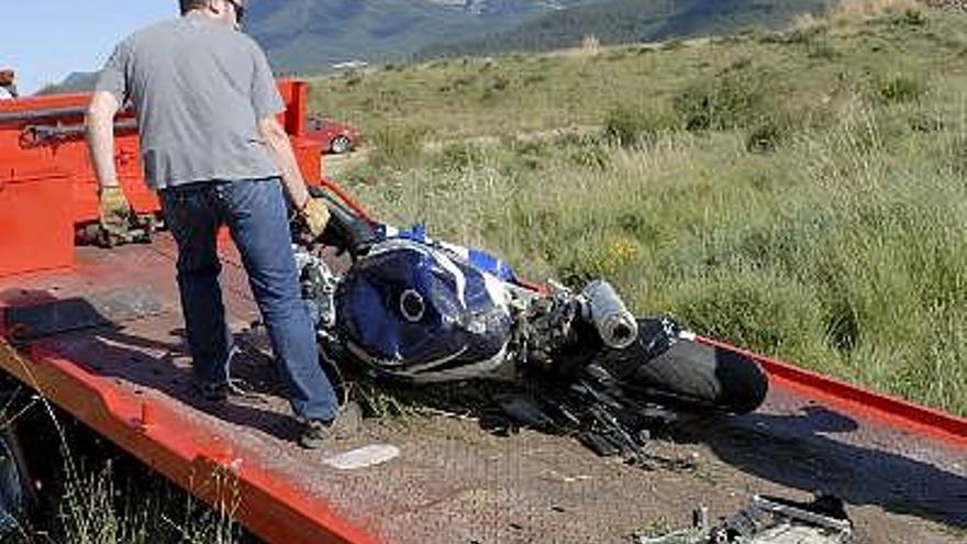 Un operario coloca en una grúa la motocileta en la que viajaban las dos personas que han fallecido hoy al salirse el vehículo de la calzada y chocar contra unas rocas en el kilómetro 2 de la carretera HU-V-2101.