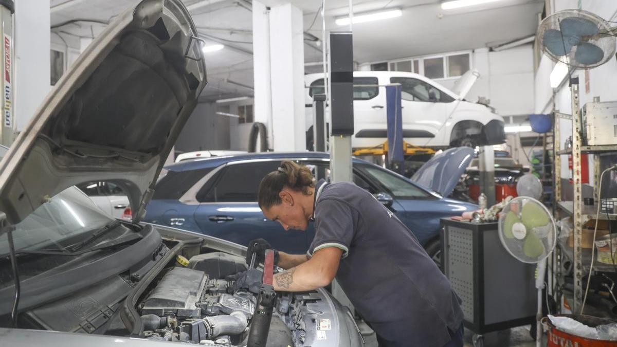 Una mecánica reparando un vehículo en el taller Alejandro Rico de Alicante, totalmente abarrotado de coches.