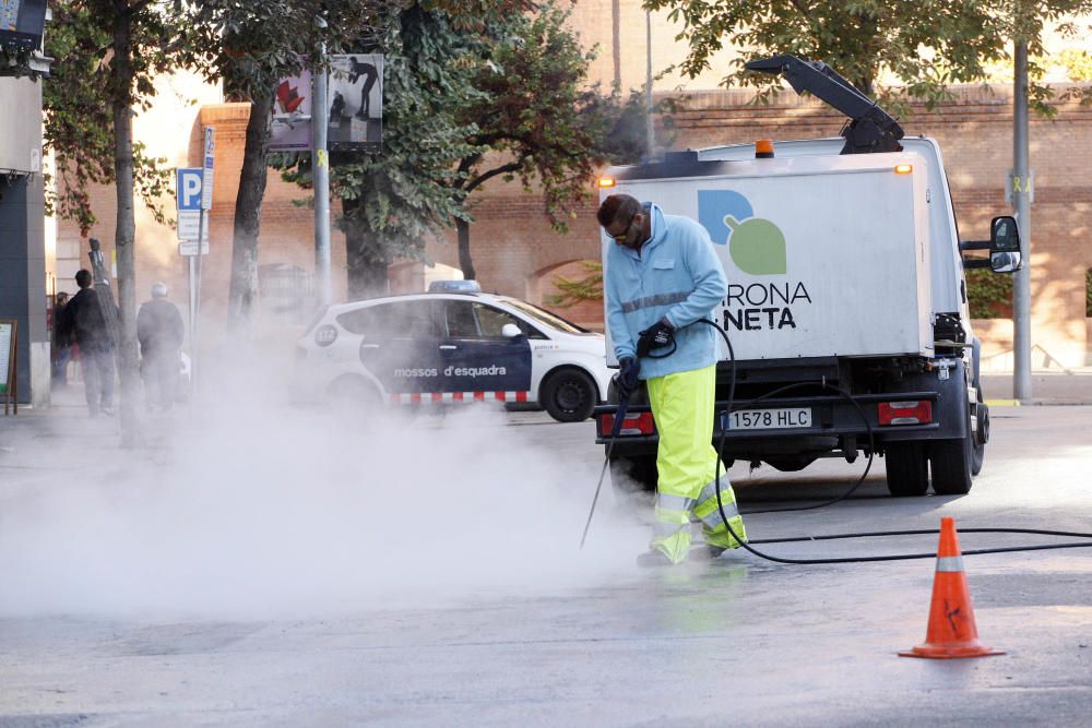 Carrers amb restes de mobiliari urbà cremat, contenidors per terra i treballadors de la brigada treballant