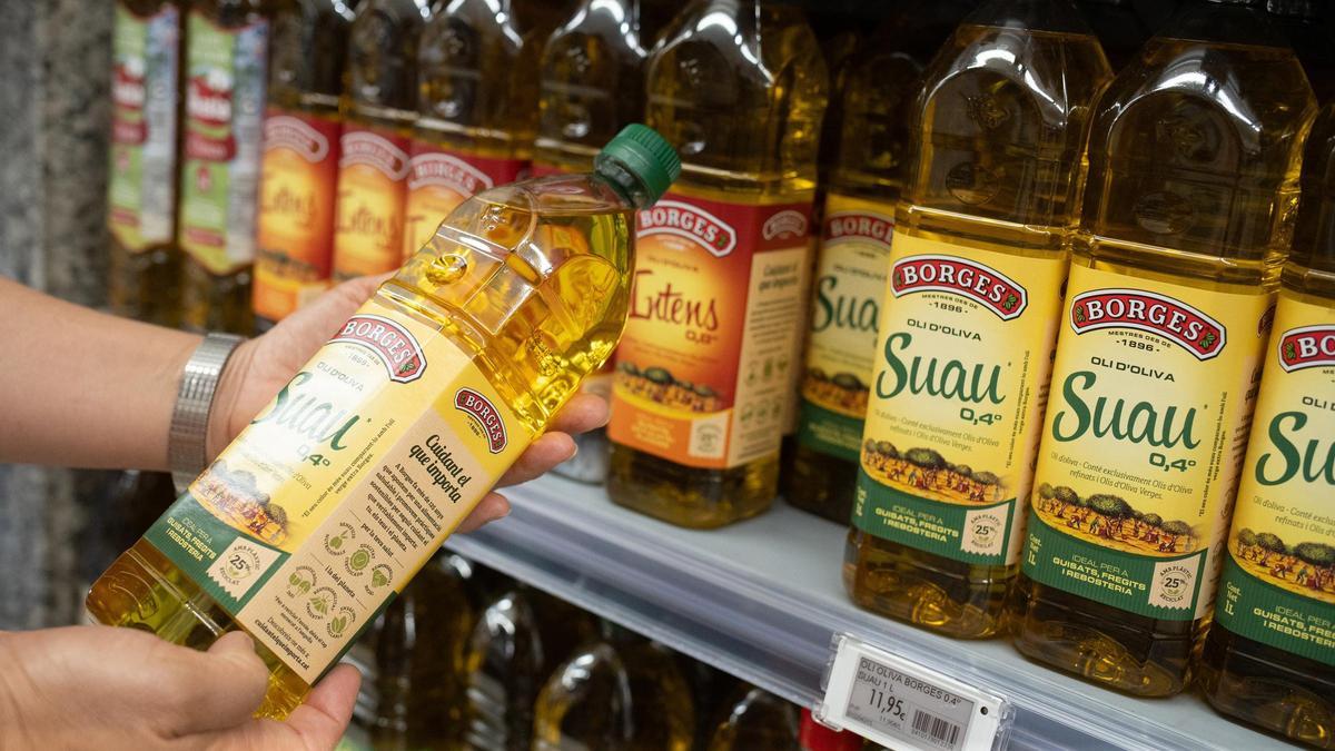 Una persona sostiene una botella de aceite  de oliva en un supermercado.