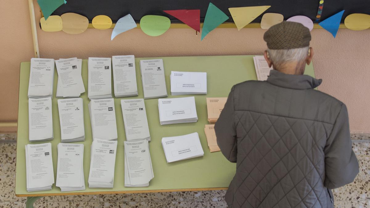 Un hombre eligiendo la papeleta de la formación política a la que quiere votar en un colegio electoral.