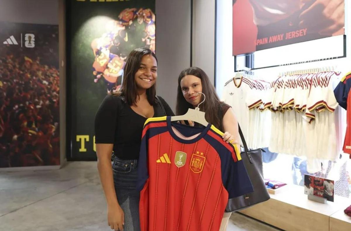 Dos chicas muestra la camiseta que este martes a puesto a la venta Adidas, con las dos estrellas y el escudo actualizado tras haber ganado el Mundial 2026.