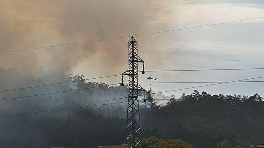 Al fondo, monte incendiado en Loureda y helicóptero.