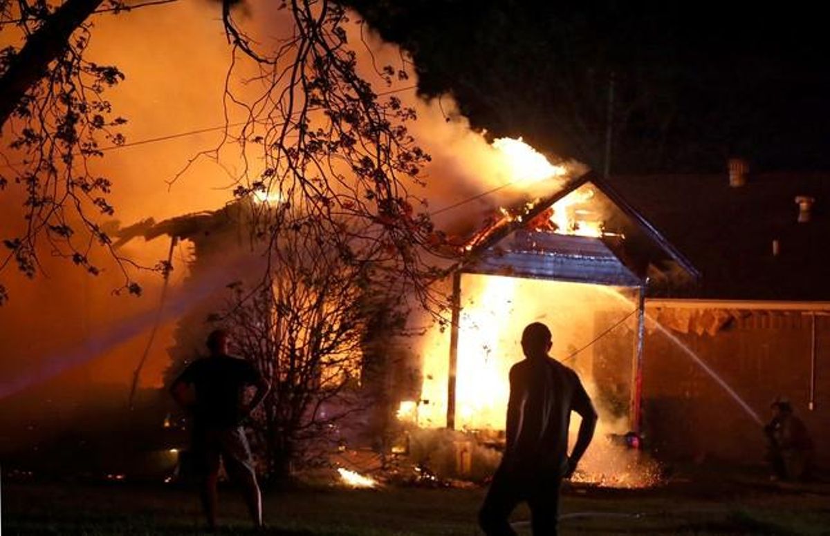 Una persona mentre els equips d’emergència intenten apagar el foc en una casa a prop de la planta fertilitzant.