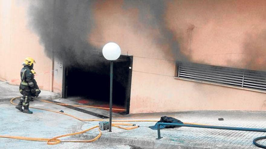 Un bombero aguarda en la puerta del garaje de la calle Rafaletes mientras el humo negro asoma por la entrada.