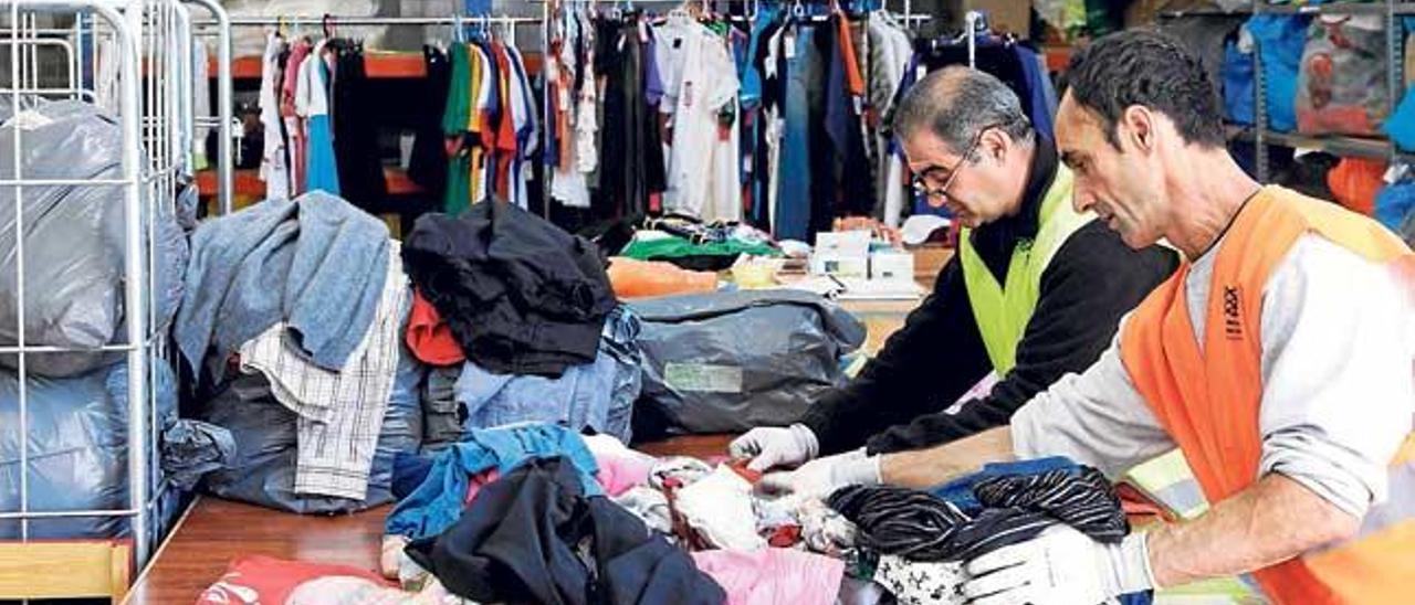 Dos personas clasifican ropa en la nave central de Deixalles.