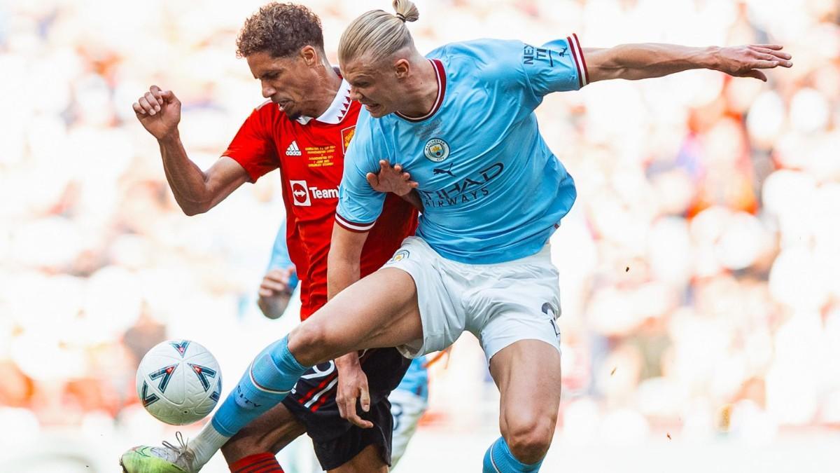 Raphael Varane y Erling Haaland luchan por un balón durante un derbi de Manchester