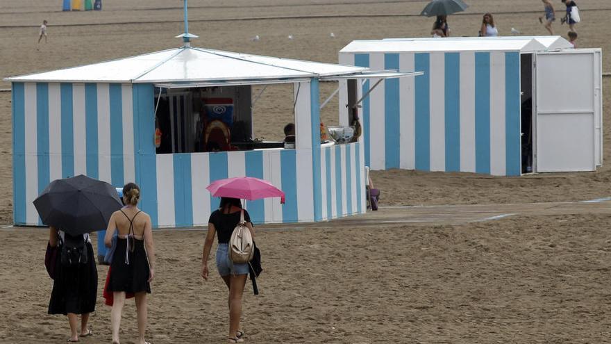 Unas jóvenes se protegen con paraguas de la lluvia en la playa de la Malva-rosa.