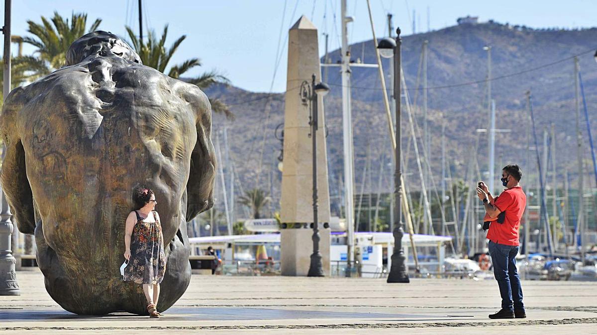 Una mujer se quita la mascarilla para fotografiarse con una estatua en Cartagena. | IVÁN URQUÍZAR