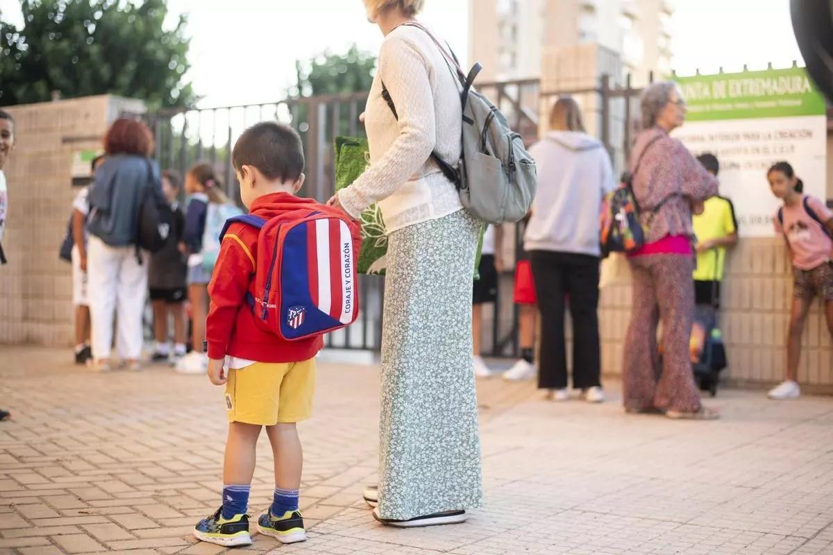 Un escolar espera junto a un familiar a la entrada del colegio en una jornada de regreso a las aulas.