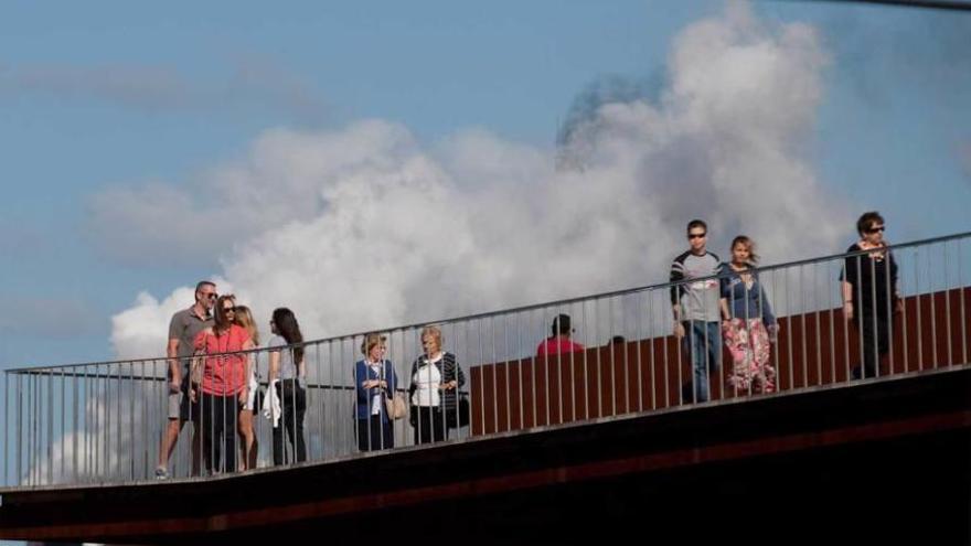 Varios peatones caminan por la Grapa con una nube de humo industrial como telón de fondo.