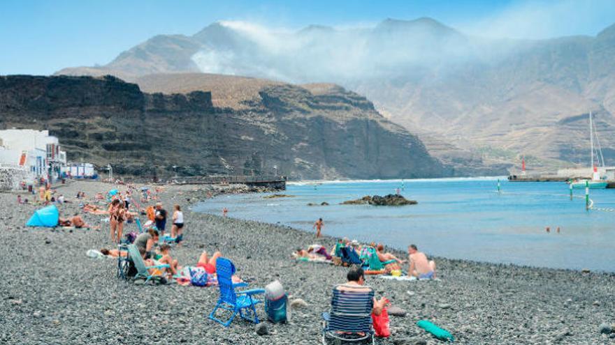 Bañistas en el puerto de Agaete mientras el fuego sigue activo en las montañas del fondo este miércoles.