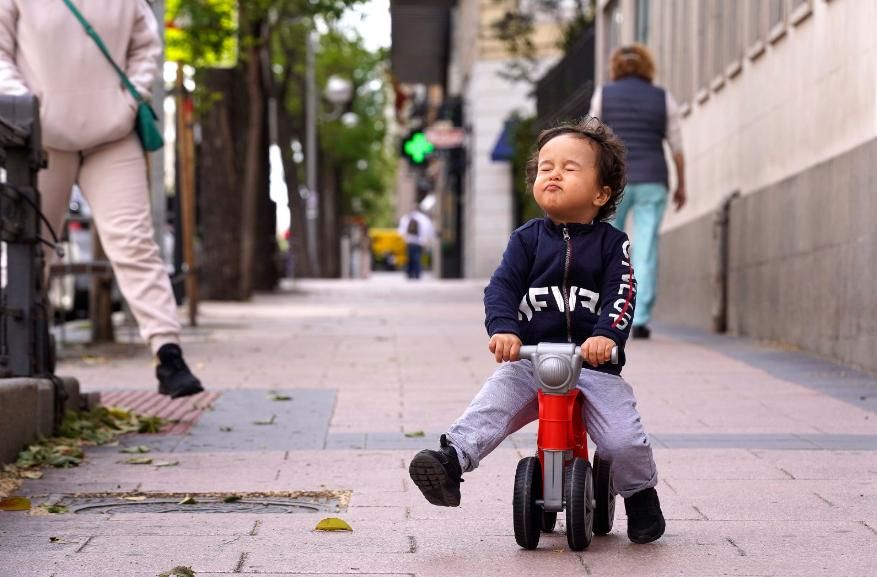 Un niño pequeño pasea por la calle con una moto de juguete, en Madrid.