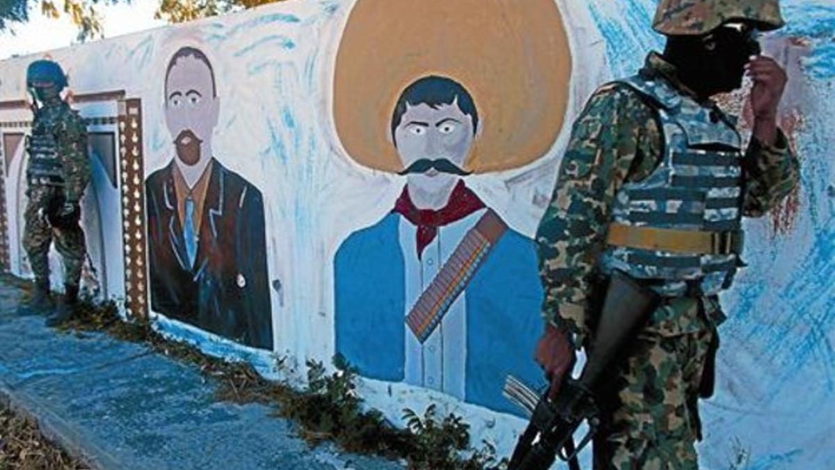 Un soldado camina frente a una pintura mural de los revolucionarios Emiliano Zapata y Francisco Madero.