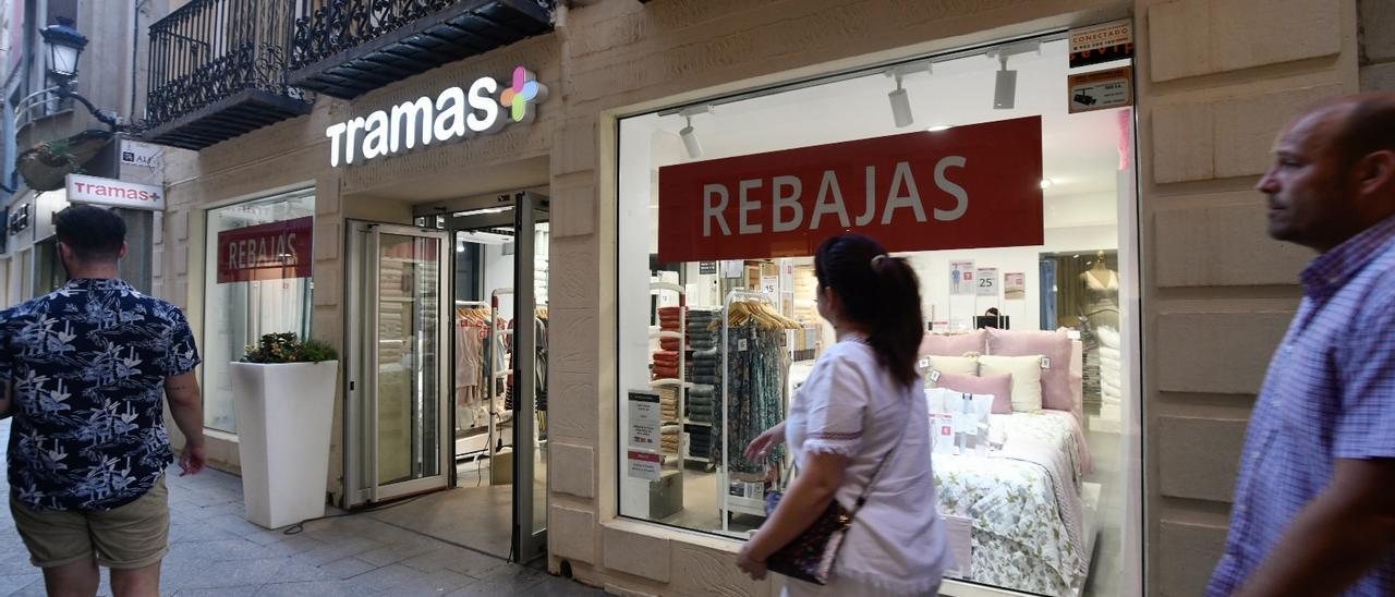 Transeúntes pasean frente al escaparate de una tienda en Murcia que ofrece rebajas y descuentos, esta tarde.