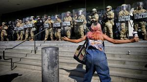 Una mujer protesta ante un cordón policial armado frente a una institución en Los Ángeles.