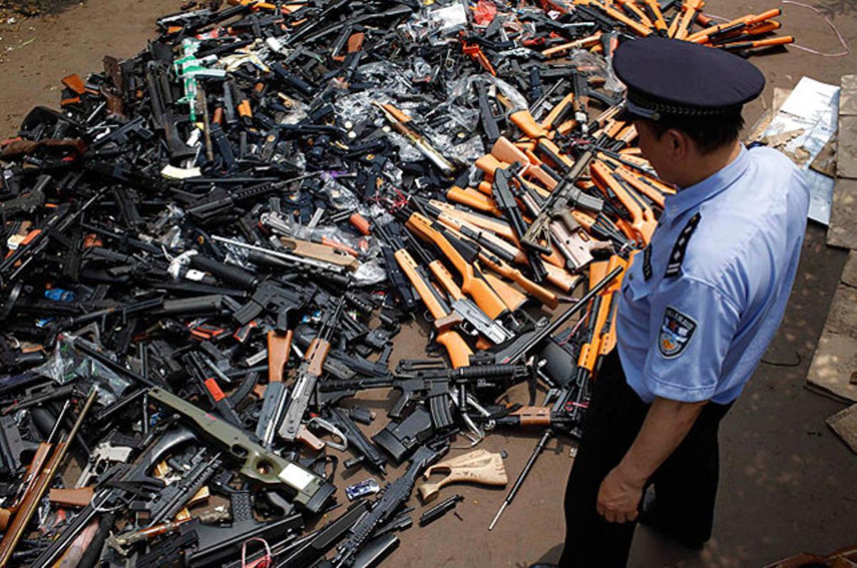 Un policía, junto a un montón de armas de juguete confiscadas antes de destruirlas, en Shanghái. Más de 100.000 armas de fuego ilegales, réplicas de pistolas, y espadas fueron destruidos en 150 ciudades de China esta semana.