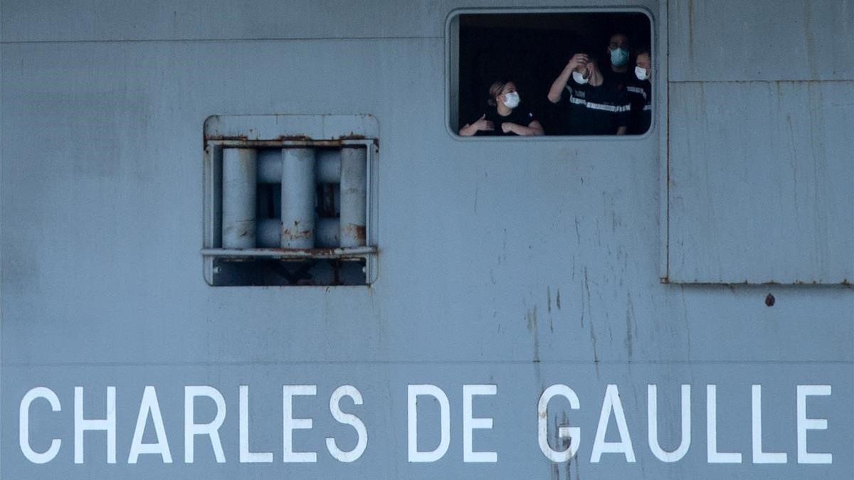 Unos marineros del 'Charles de Gaulle' con mascarillas se asoman por una ventana del portaaviones.