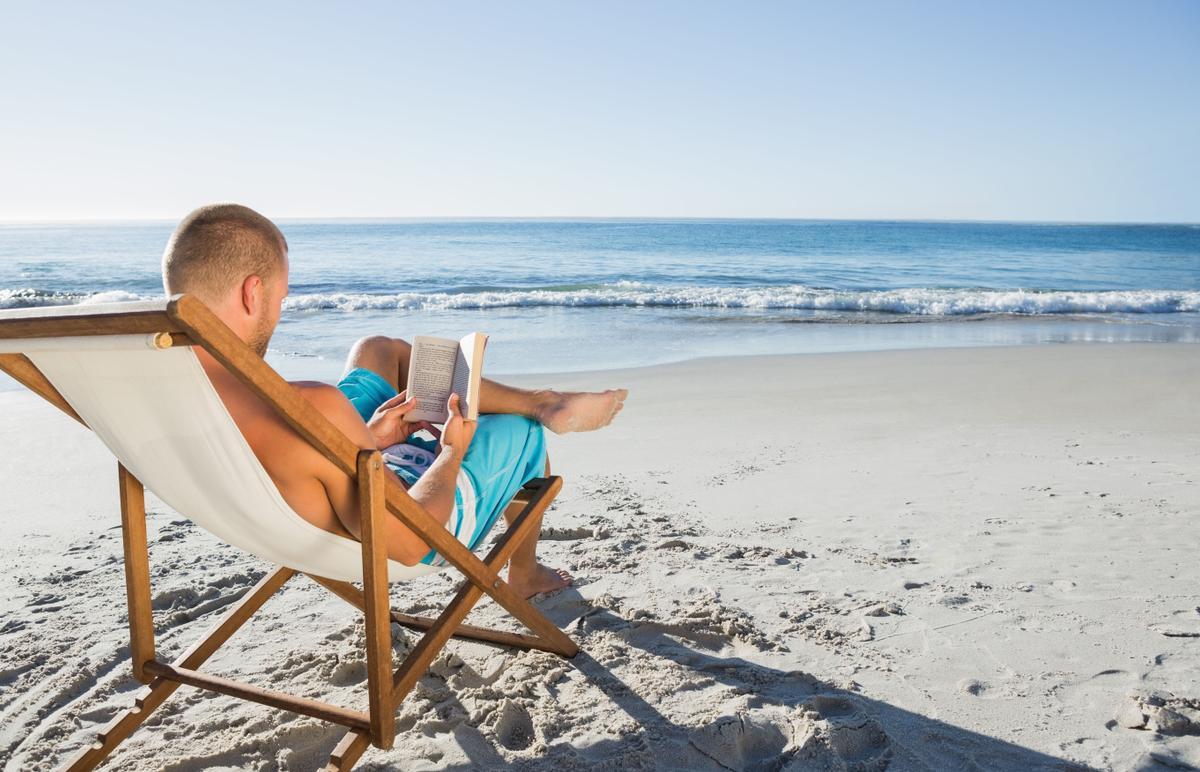 Un hombre leyendo un libro en la playa. 