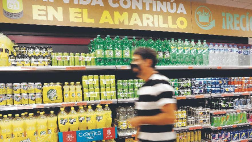 Un cliente pasa por delante del lineal de refrescos donde se observa un cartel que explica dónde depositar estos envases.