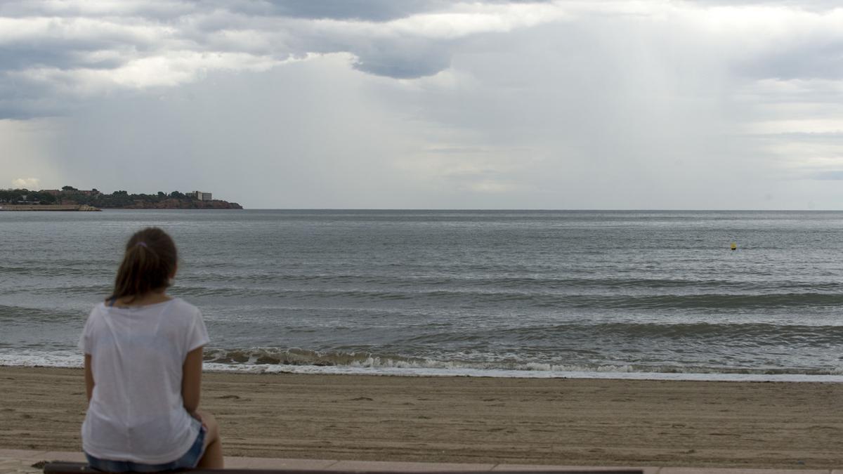 Una mujer mira el cielo que amenaza lluvia en la playa del Arenal, en L'Ampolla (Baix Ebre).