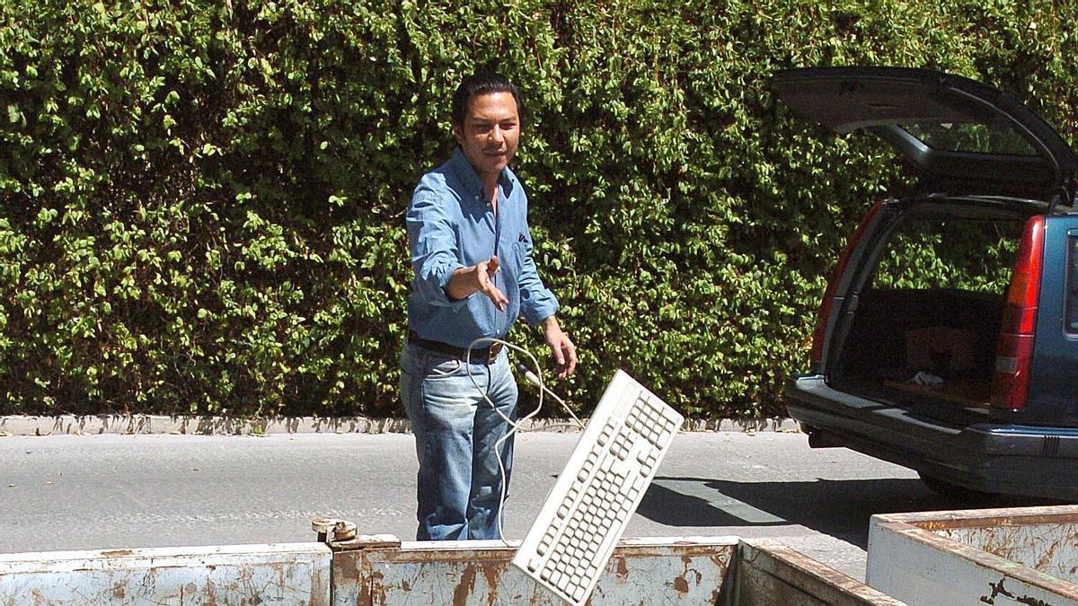 Un hombre tira un teclado de ordenador a un punto limpio de residuos electrónicos.a