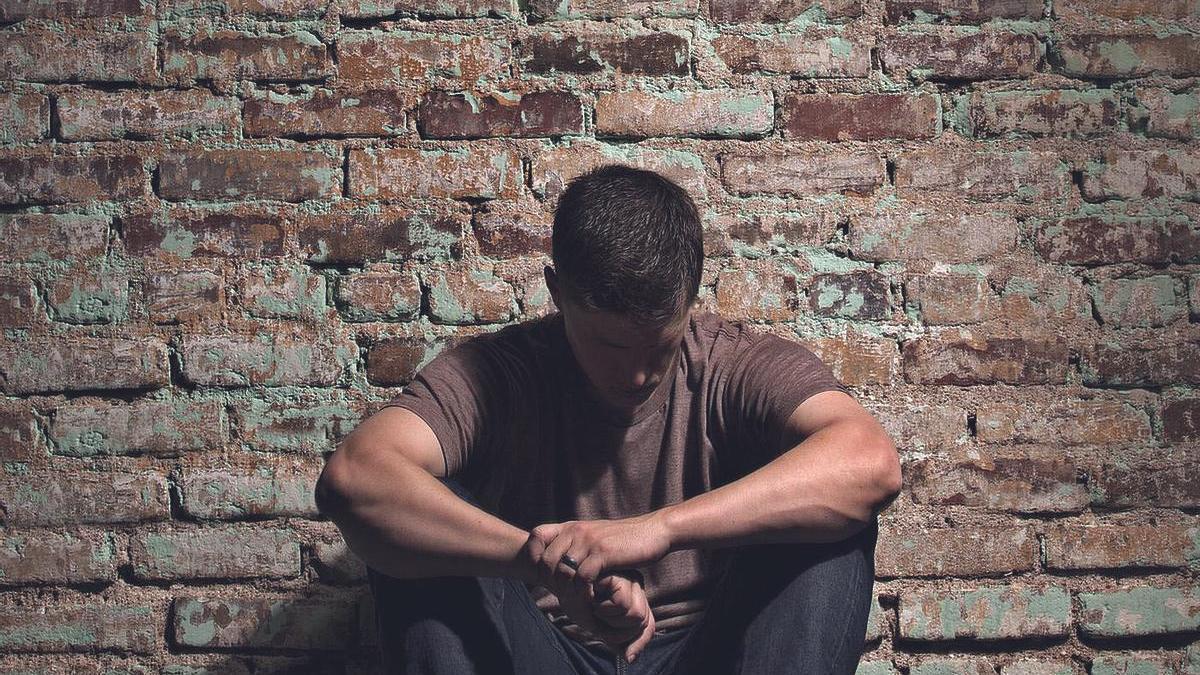 Depressed man sitting alone against brick wall.