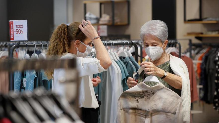 Una mujer es atendida por una dependienta en un comercio.