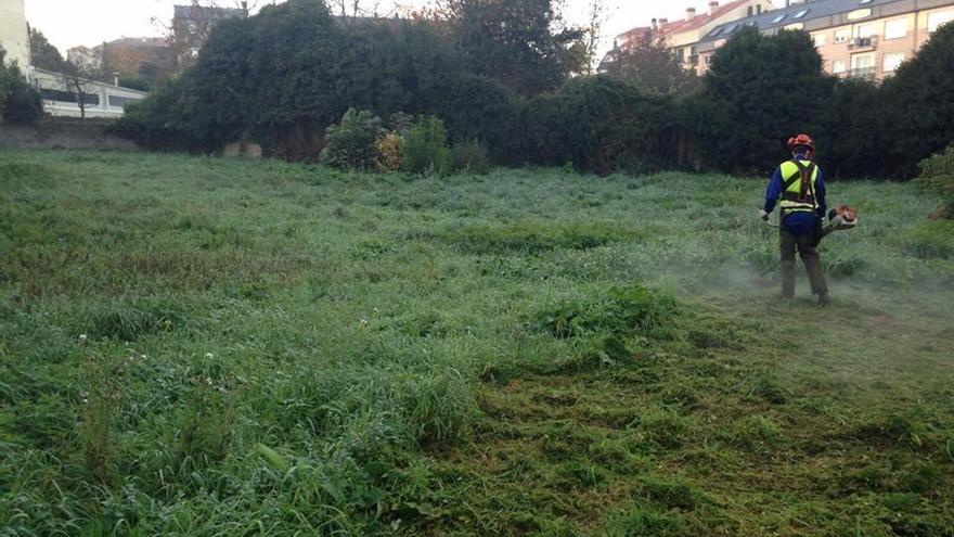 Un operario realiza tareas de siega de hierba y desbroce de maleza en el solar situado detrás de las casas de maestros del colegio Xesús Golmar.