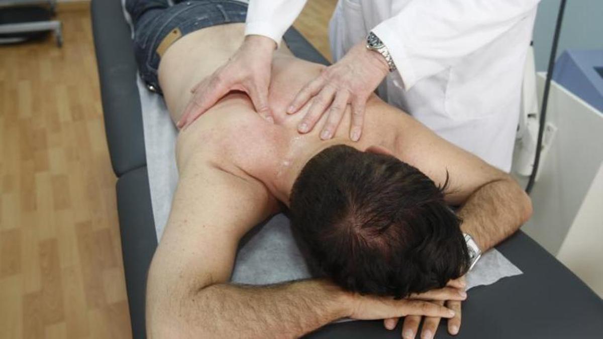 Un fisioterapeuta atiende a un paciente sobre una camilla.
