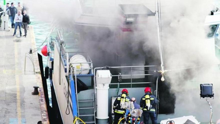 Agentes de Bomberos acceden al barco «Rey de Olalla», aún humeante, a su llegada al puerto de Burela.