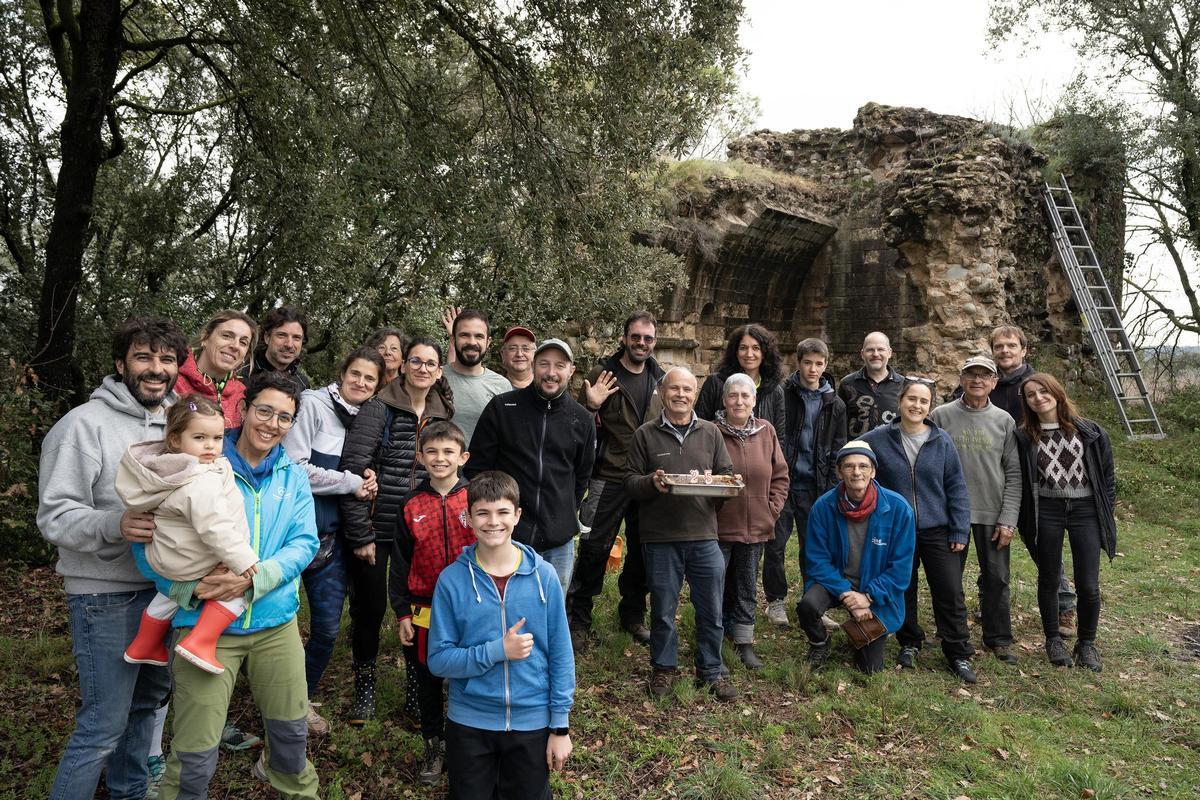 Els voluntaris que fa uns dies van participar a la 25a neteja anual del castell de Navata, al fons, organitzada pels Amics de Navata.