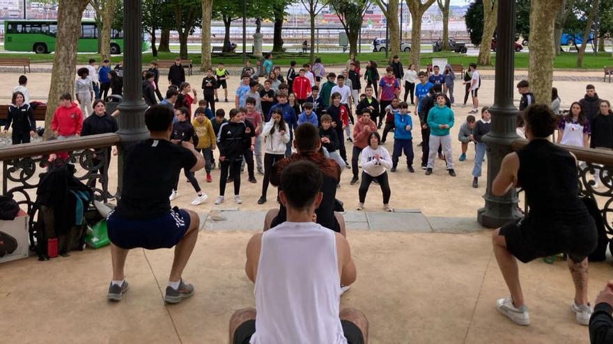 Arriba, un grupo de futuros monitores de gimnasio muestra un ejercicio de fitness en el kiosco de la música del muelle mientras el alumnado del IES de La Magdalena lo pone en práctica. A la izquierda, alumnos del instituto en plena batalla del juego del pañuelo. | F. L. J. / I. G.